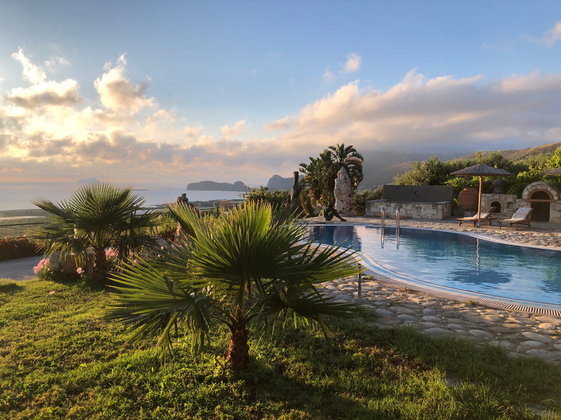 The infinity pool at golden hour — palm, cobblestone, Gramvousa island and Falassarna Bay beyond